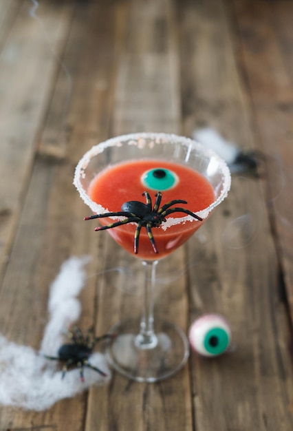 Aterrador cocktail vermelho com aranha em fundo de madeira para Halloween com decoração