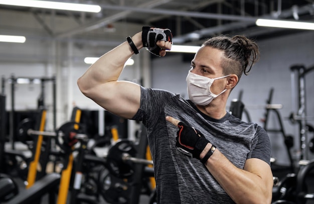 Athlet, der während einer Pandemie im Fitnessstudio trainiert und eine schützende Gesichtsmaske trägt