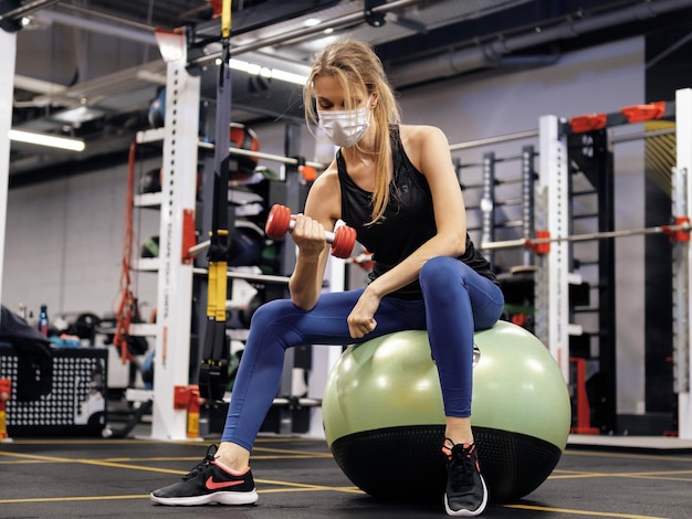 Athlet, der während einer Pandemie im Fitnessstudio trainiert und eine schützende Gesichtsmaske trägt