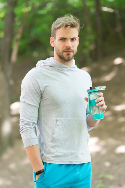 Athlet hält Plastikflasche an der frischen Luft Durst Macho Entspannen Sie sich mit einer Wasserflasche nach dem Training im Park Entspannen Sie sich im Wald Bleiben Sie hydratisiert und gesund Wasser ist Teil eines gesunden Trainings Sport und Fitness