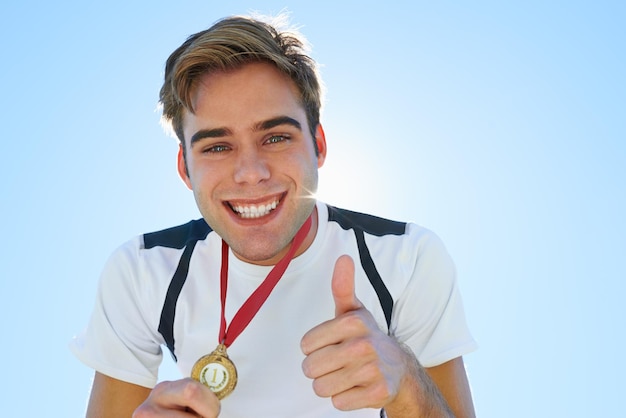 Foto athlet mann und daumen nach oben mit medaille für sportliche leistungen erfolg porträt und ja im wettbewerb gesicht des gewinners oder läufer mit wie lächeln oder guten job hände emoji und goldpreis auf einem blauen himmel