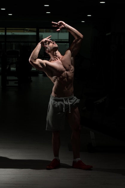 Athlet muskulöser brutaler Bodybuilder emotionales Posieren in einem dunklen Fitnessstudio