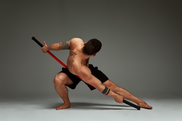 Athleten mit Stocktraining Karate mit Sportwerkzeug im Studio auf grauem Hintergrund