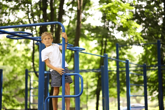 Athletenjunge im Park macht Sport, hängt an seinen Händen und macht Übungen auf den Stufenbarren mit gekreuzten Beinen