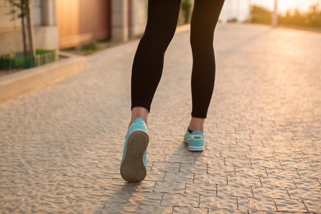 Athletenläuferfüße, die auf Straßennahaufnahme auf Schuh laufen. Frau Fitness Sonnenaufgang Joggen Workout Wellness-Konzept.