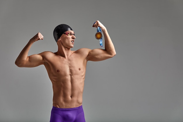 Athletenschwimmer mit einer Medaille in seinen Händen, die einen Kopienraum des grauen Hintergrundes des Sieges feiern