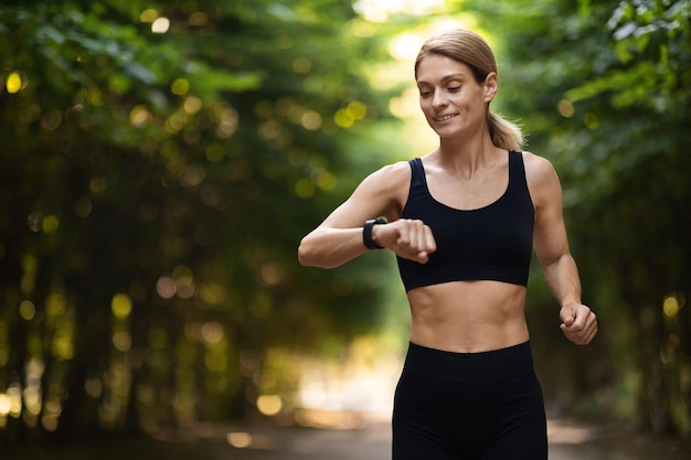 Athletische blonde Frau, die beim Laufen im Freien Fitnessarmband anschaut