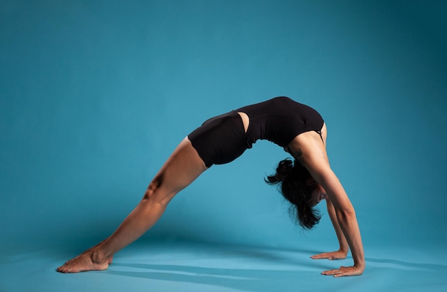 Athletische Fitnessfrau, die in Brückenposition steht, trainiert die Ausdauer des Körpers und arbeitet an einem gesunden Lebensstil im Studio mit blauem Hintergrund. Persönlicher Trainer, der Körperhaltung ausübt