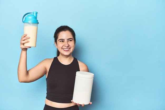 Athletische Frau hält einen Proteinshake und ein Glas in der Hand