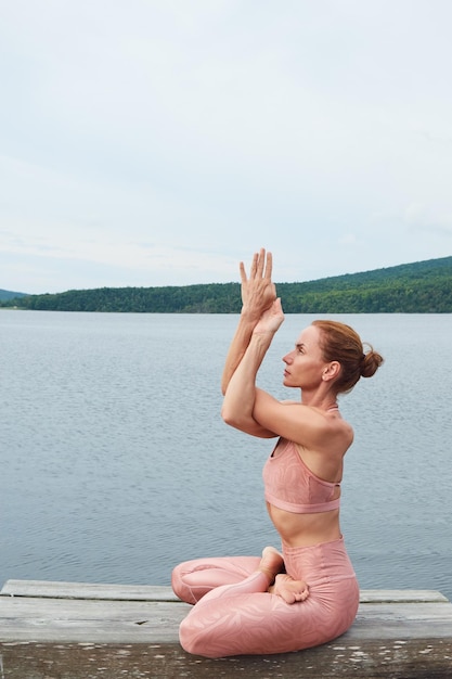 Athletische Frau in rosafarbener Sportbekleidung, die im Lotussitz sitzt und Yoga im Freien praktiziert