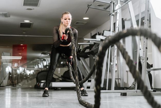 Athletische Frau mit Kampfseil, die im Fitnessstudio trainiert