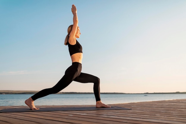 Athletische Frau mittleren Alters, die im Freien Yoga auf einem Holzsteg praktiziert