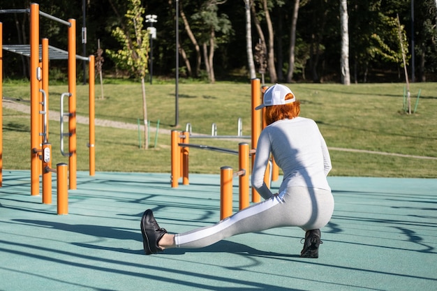 Athletische Ingwerfrau, die sich im sonnigen Herbst für das morgendliche Training im Freien auf dem städtischen Sportplatz aufwärmt...