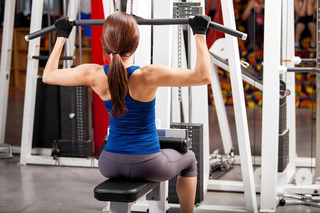 Athletische junge Frau, die einige Gewichte hebt und Muskeln in einem Fitnessstudio aufbaut
