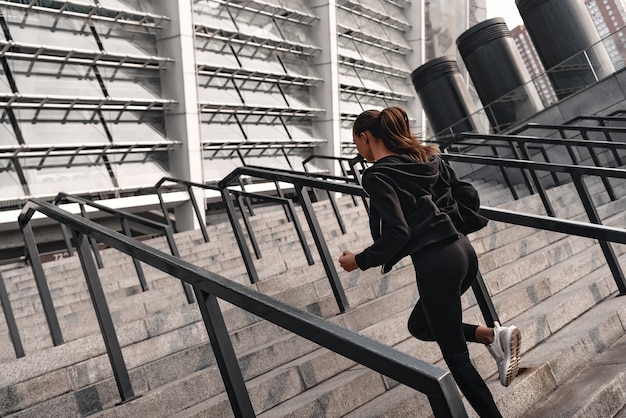 Athletische junge Frau, die oben läuft. Sie trägt Sportkleidung und weiße Turnschuhe.