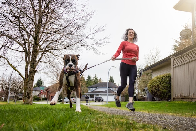 Athletische kaukasische erwachsene Frau, die draußen mit einem Boxer-Hund läuft