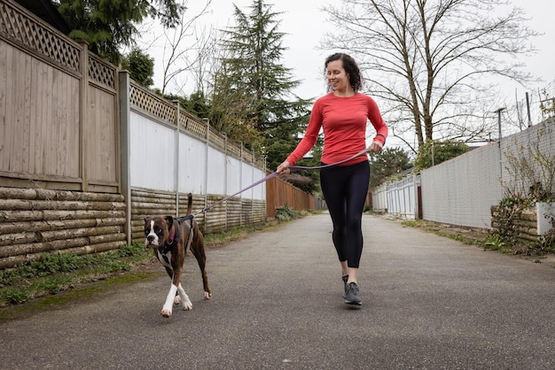 Athletische kaukasische erwachsene Frau, die draußen mit einem Boxer-Hund läuft