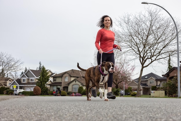 Athletische kaukasische erwachsene Frau, die draußen mit einem Boxer-Hund läuft