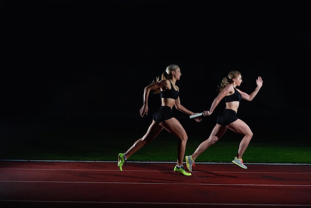 athletische läuferinnen, die den stab im staffellauf übergeben