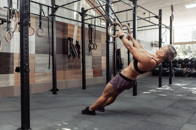 Athletische Sportfrau, die mit Turnringen in der modernen Kreuzturnhalle trainiert