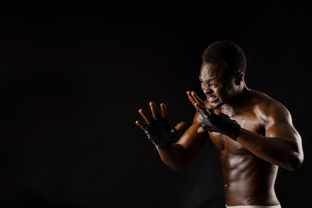 Athletischer afrikanischer Kämpfer auf schwarzem Hintergrund. Dunkelhäutiger unbekleideter Mann zeigt einen Kampf. Werbung für Sportverein und Fitnessstudio. Professionelles Boxen und Karate.
