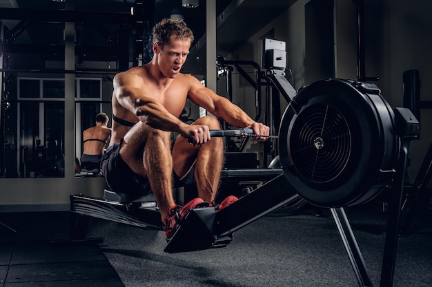 Athletischer, hemdloser Mann, der in einem Fitnessstudio auf dem Rücken mit einem Krafttrainingsgerät trainiert.