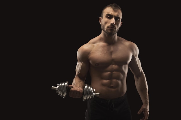 Athletischer junger Mann mit Hantel auf schwarzem Hintergrund. Nackter Oberkörper, muskulöser Körper. Starke Brust- und Schultermuskulatur. Studioaufnahme, Bodybuilding-Konzept, Kopierraum