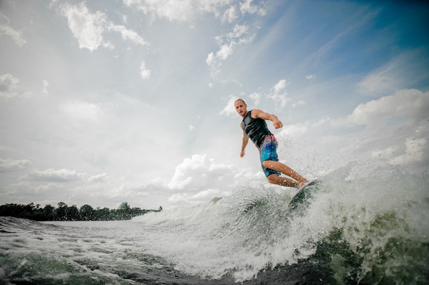 Athletischer Mann, der auf dem Brett hinunter den Fluss gegen den Himmel wakesurfing ist