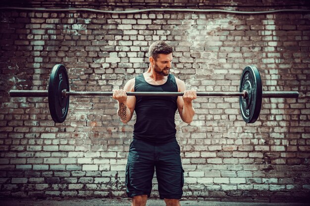 Athletischer Mann, der mit einem Barbell ausarbeitet. Kraft und Motivation. Bizeps-Übung.