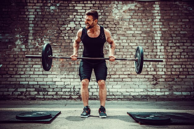 Athletischer Mann, der mit einem Barbell ausarbeitet. Kraft und Motivation. Übung für die Rückenmuskulatur