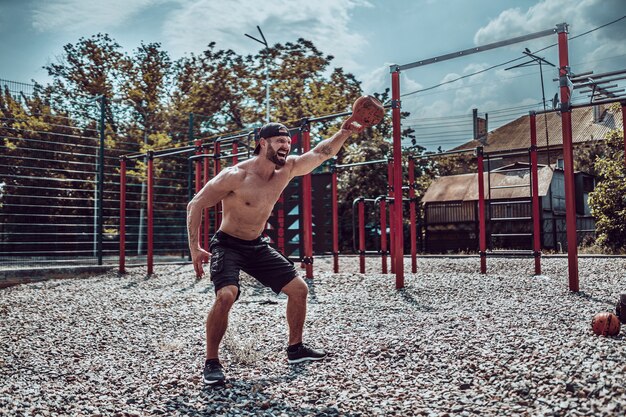 Athletischer Mann, der mit einer Kettlebell am Straßengymnastikhof ausarbeitet