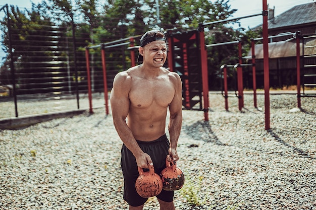 Athletischer Mann, der mit einer Kettlebell am Straßengymnastikhof ausarbeitet