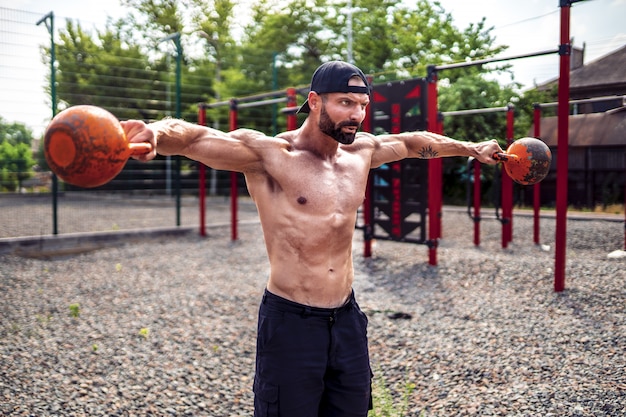 Athletischer Mann, der mit einer Kettlebell am Straßengymnastikhof ausarbeitet