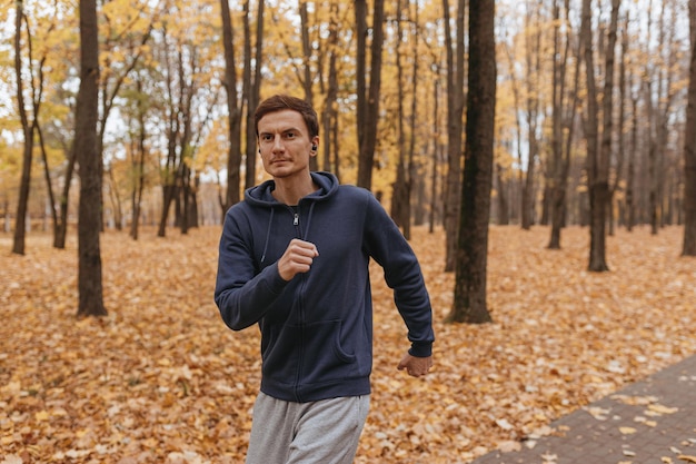 Athletischer Mann, der Musik in Kopfhörern hört und im Park läuft, während er am Herbsttag trainiert