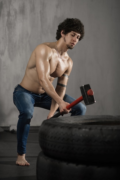 Athletischer Mann schlägt Reifen - Training an der Turnhalle mit Hammer