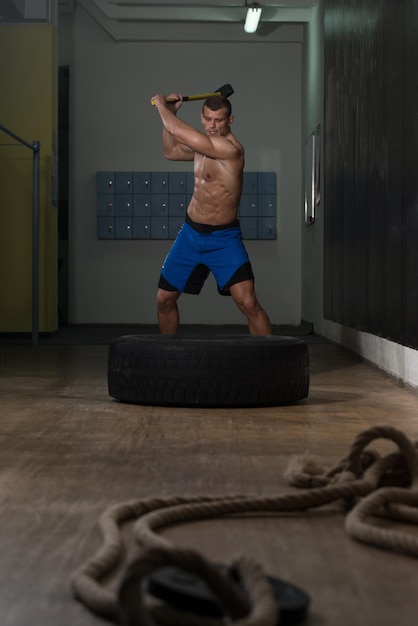 Foto athletischer mann trifft reifentraining im fitnessstudio mit hammer und traktorreifen