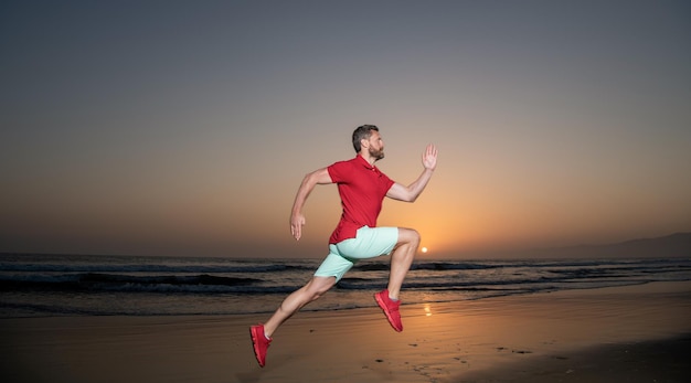 Athletischer Mannläufer, der auf Sonnenuntergangsommer-Strandherausforderung läuft
