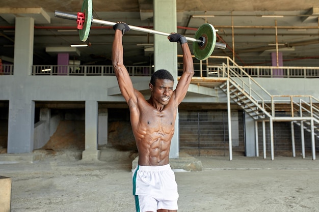 Athletischer schwarzer junger Mann, der eine schwere Langhantel im Fitnessstudio im Freien unter der Brücke hebt Gesundes Lebensstilkonzept