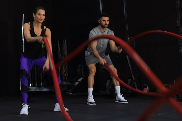 Athletisches junges Paar mit Kampfseil beim Training im Fitness-Studio für funktionelles Training.