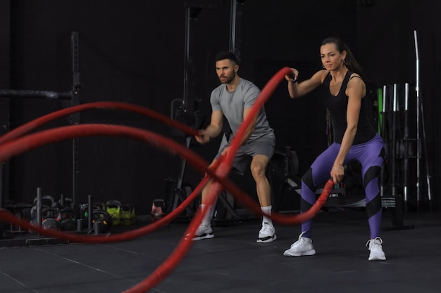 Athletisches junges Paar mit Kampfseil beim Training im Fitness-Studio für funktionelles Training