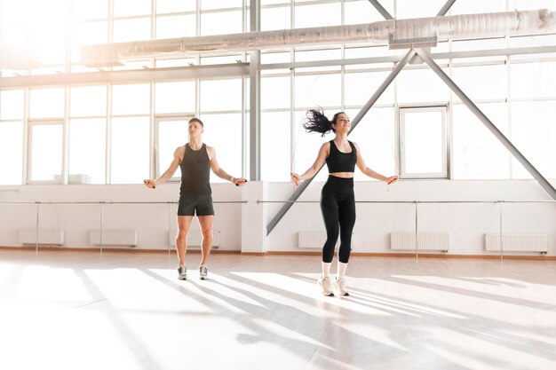 Athletisches Paar in Sportbekleidung springt morgens im Fitnessstudio Seil, Fitness-Mädchen und Trainer-Mann
