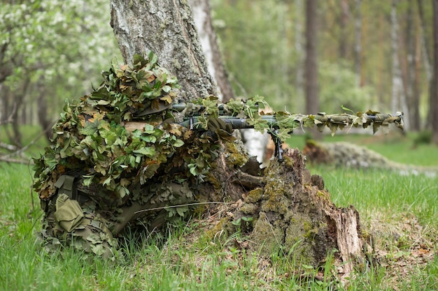 Atirador camuflado na floresta em emboscada. Militar apontando uma arma, um rifle para o inimigo na natureza