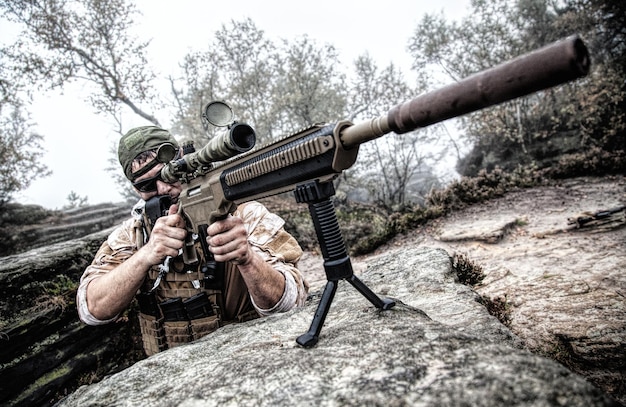 Atirador militar privado PMC com boné de beisebol e rifle de assalto nas rochas