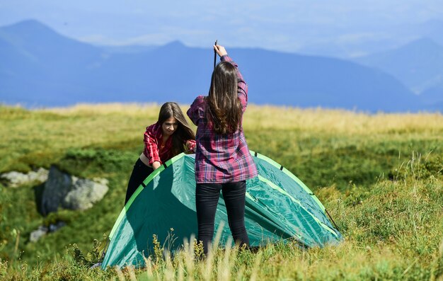 Atividade de caminhada. Anexe a tenda de componentes estruturais necessários. Prepare-se para a noite. Conceito de escuteira. Caminhadas em acampamento. Útil ter um parceiro para levantar a tenda. Mulheres montam barracas no topo da montanha.