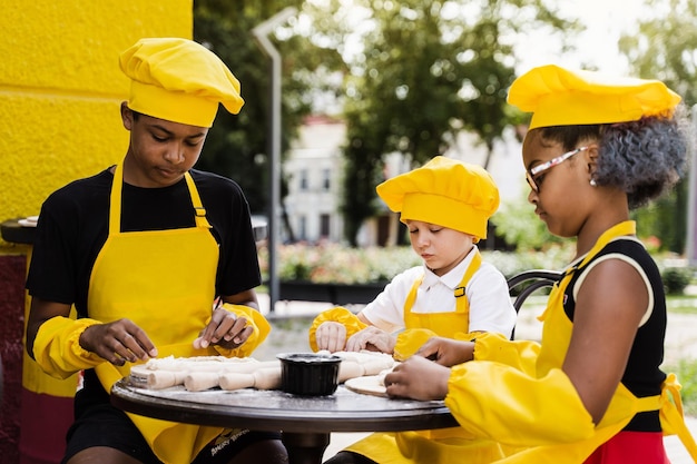 Atividade de cozinhar na infância de crianças multinacionais de crianças negras africanas e caucasianas Empresa feliz de crianças multiétnicas cozinhando massa