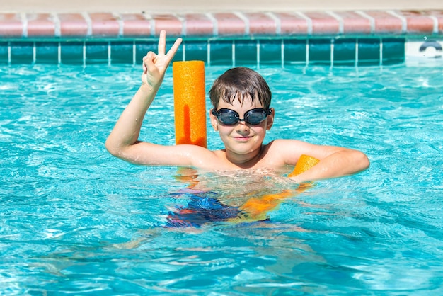 Foto atividade de verão ao ar livre conceito de diversão saúde e férias menino sorridente feliz oito anos de idade em óculos de natação nadar na piscina com macarrão em dia quente de verão