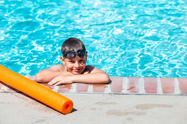 Foto atividade de verão ao ar livre conceito de saúde divertida e férias um menino feliz de oito anos de idade em óculos de natação está segurando a beira da piscina em um dia quente de verão