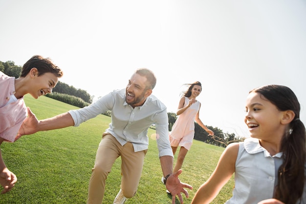 Atividades de fim de semana, pai feliz tentando pegar seus filhos e sorrindo enquanto passa o tempo livre