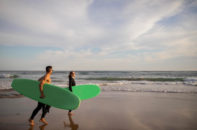 Atividades de verão casal jovem feliz carregando pranchas de surf caminhando ao longo da costa