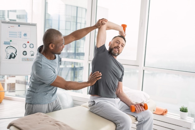 Atividades esportivas. agradável homem adulto fazendo exercícios com halteres durante uma visita ao centro de reabilitação